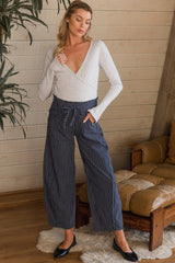 woman wearing a light gray long sleeve maternity top and navy striped wide-leg maternity pants, standing in a casual pose
