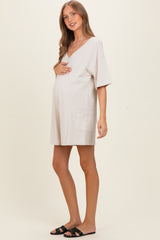 woman wearing a light beige maternity dress with short sleeves and a pocket, gently holding her baby bump