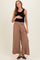 woman wearing a black ribbed tank top and brown maternity wide-leg pants, holding her baby bump