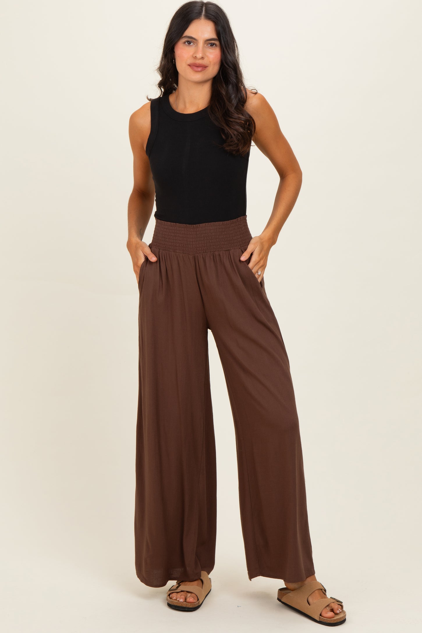 woman wearing a black sleeveless top and brown wide-leg pants with a smocked waistband