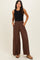 woman wearing a black sleeveless top and brown wide-leg pants with a smocked waistband