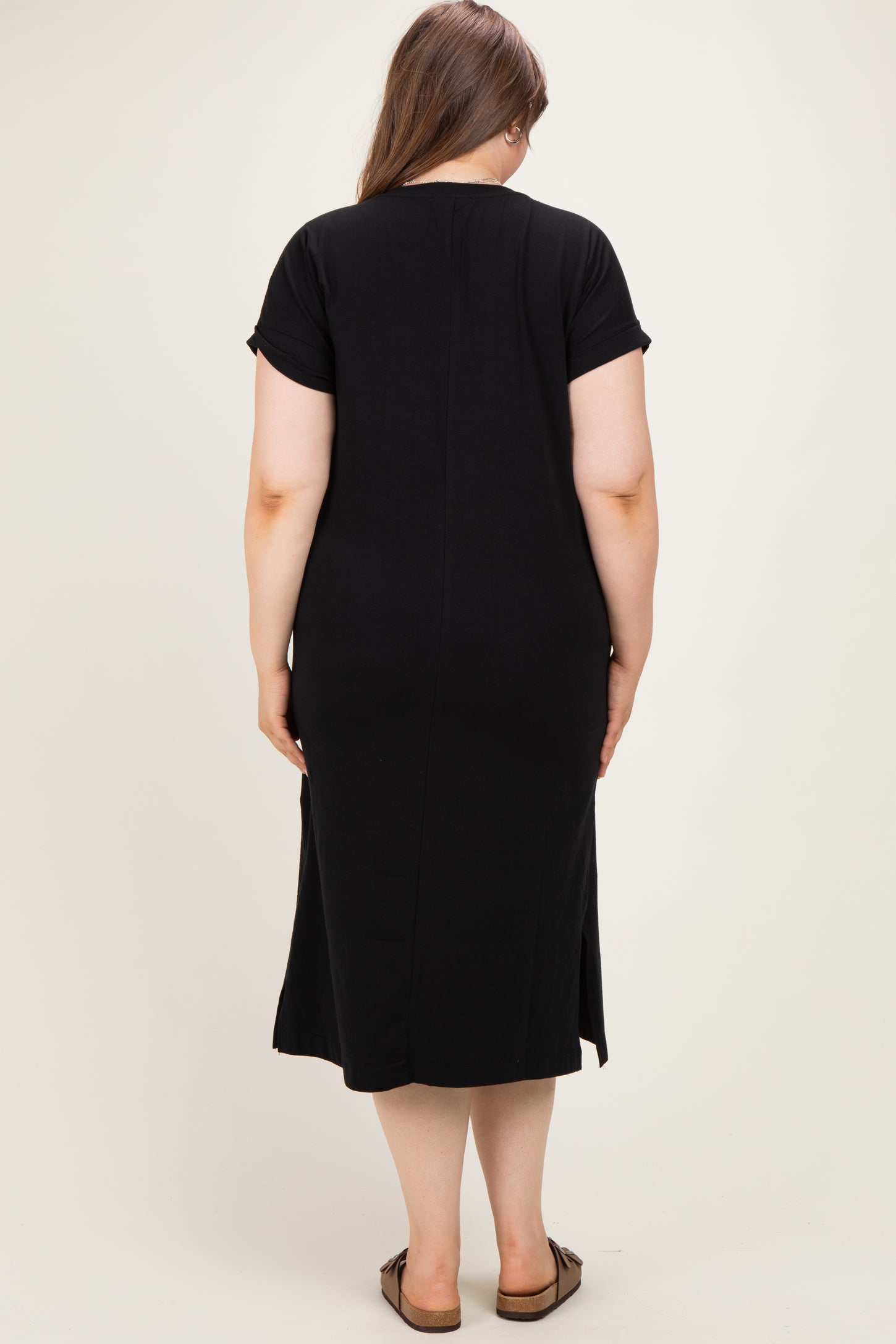 woman wearing a black maternity plus short sleeve dress, seen from the back, with a relaxed fit and knee-length hem