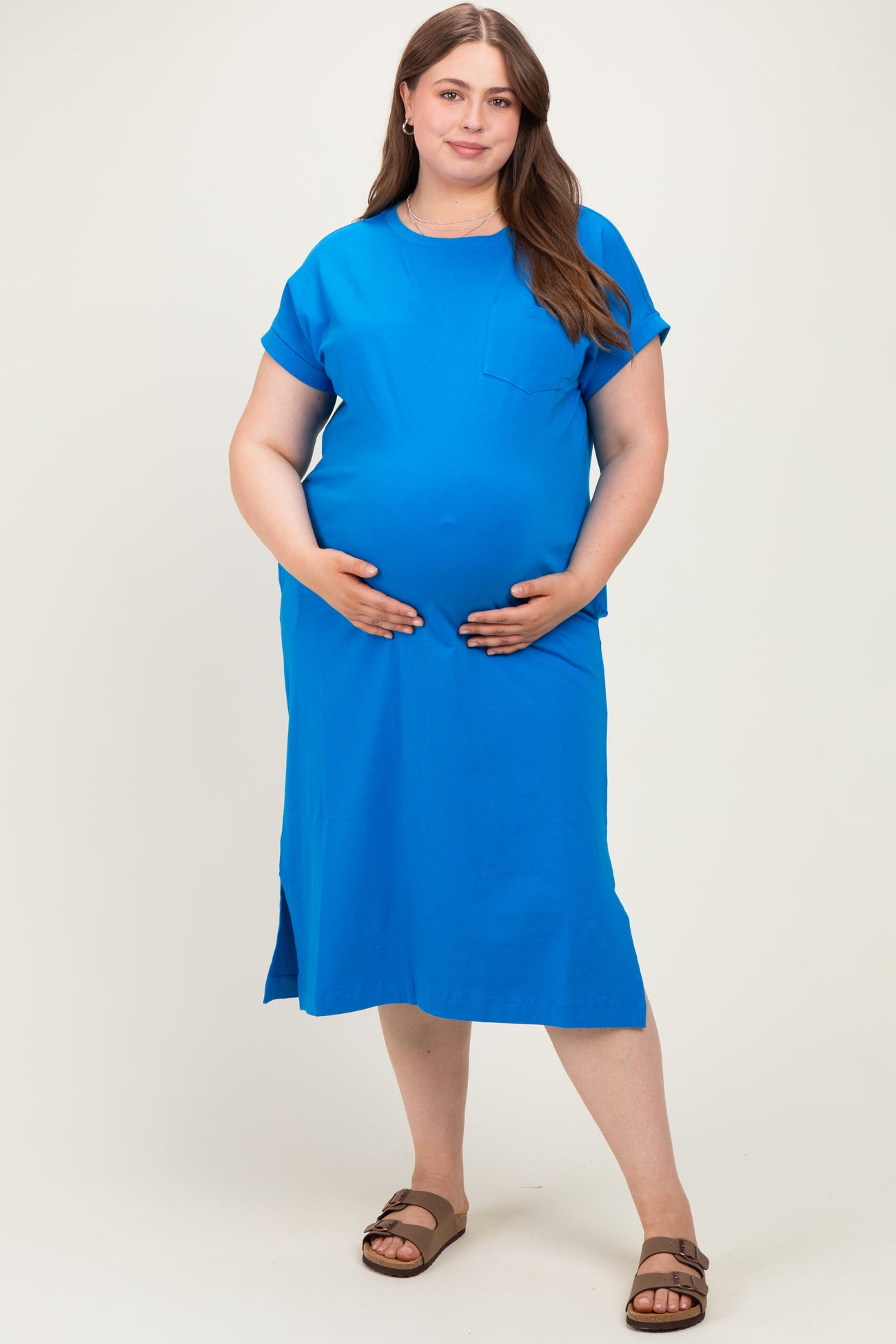 woman wearing a bright blue short sleeve maternity dress with a pocket, gently cradling her baby bump