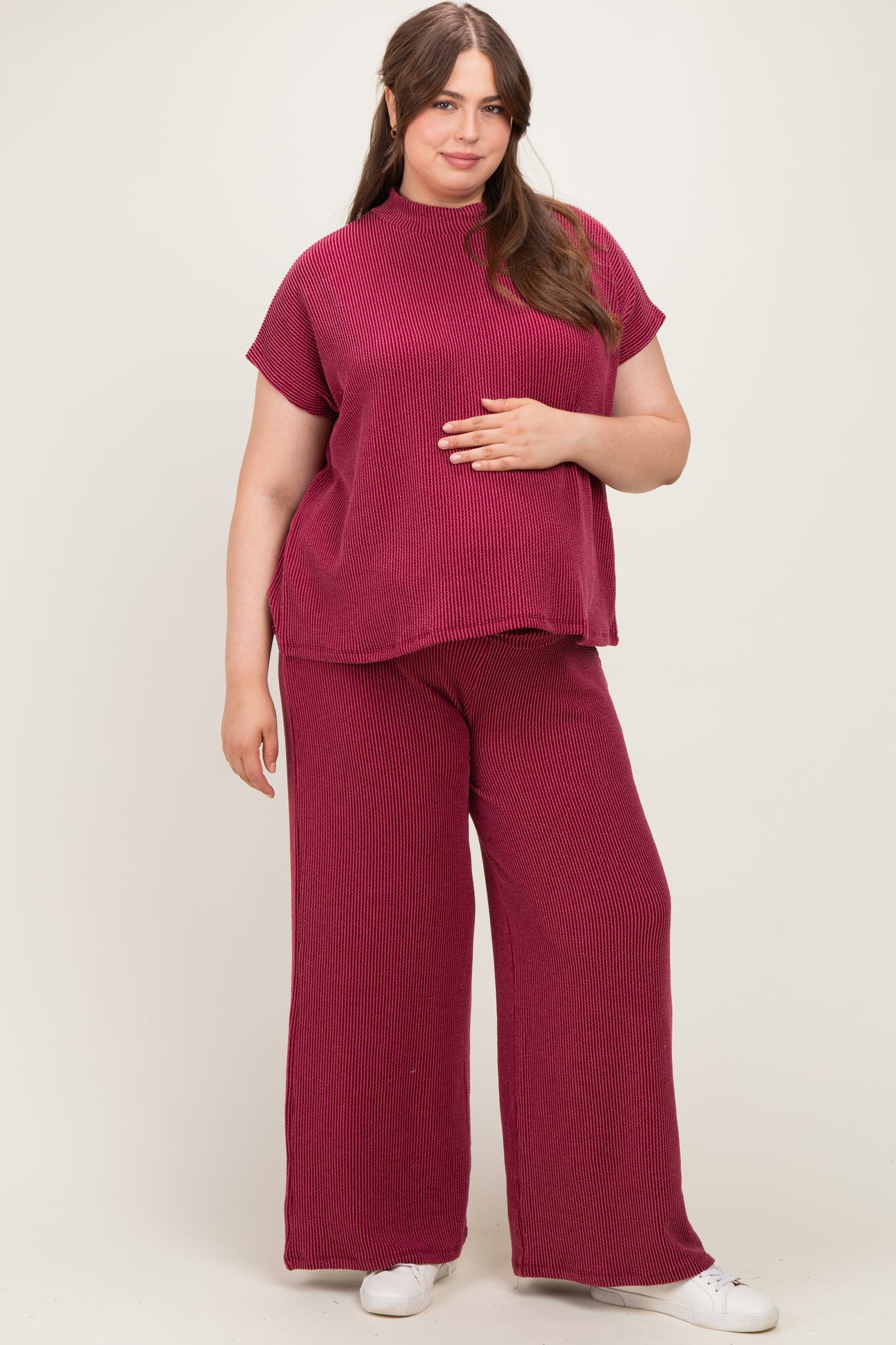 woman wearing a burgundy ribbed maternity top and wide-leg pants, holding her baby bump