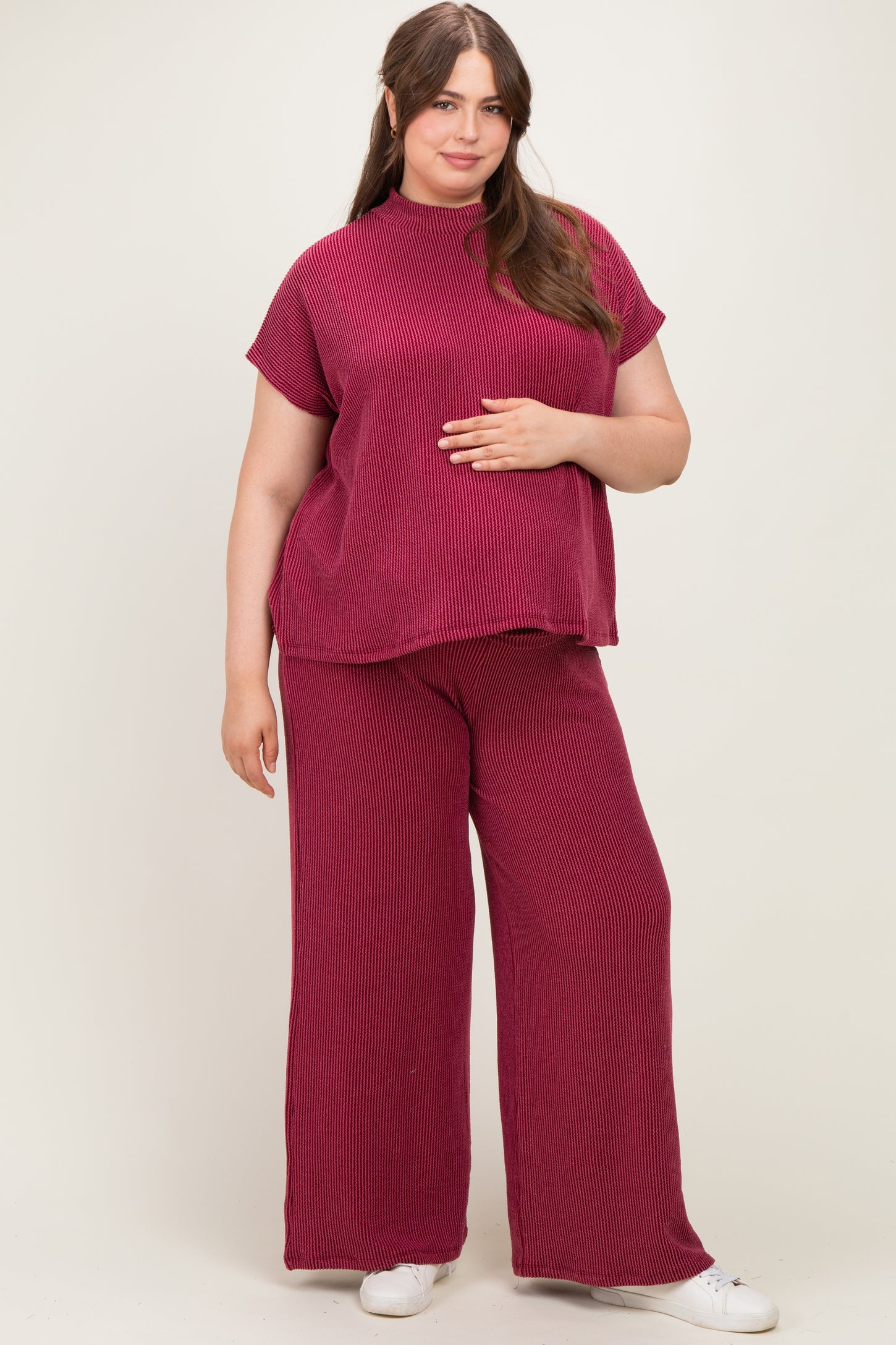 woman wearing a burgundy ribbed maternity top and wide-leg pants, holding her baby bump