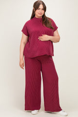 woman wearing a burgundy ribbed maternity top and wide-leg pants, holding her baby bump