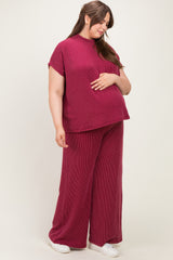 woman wearing a burgundy short sleeve maternity top and wide leg pants, gently cradling her baby bump