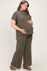 woman wearing a green ribbed maternity plus two-piece set, gently cradling her baby bump