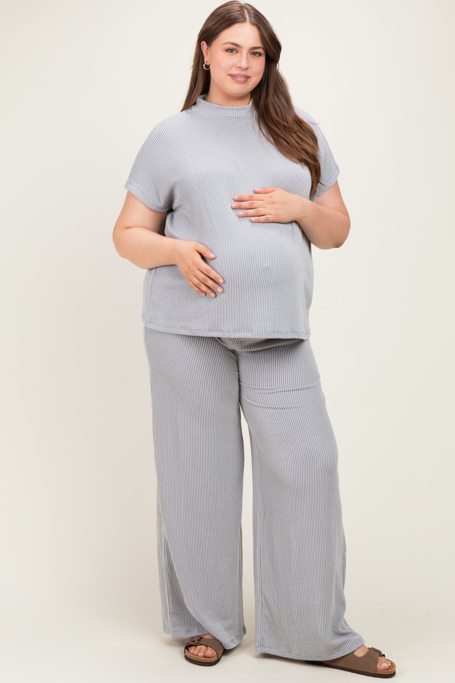 woman wearing a striped light gray maternity top and matching wide-leg pants, gently holding her baby bump