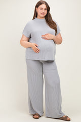 woman wearing a striped light gray maternity top and matching wide-leg pants, gently holding her baby bump