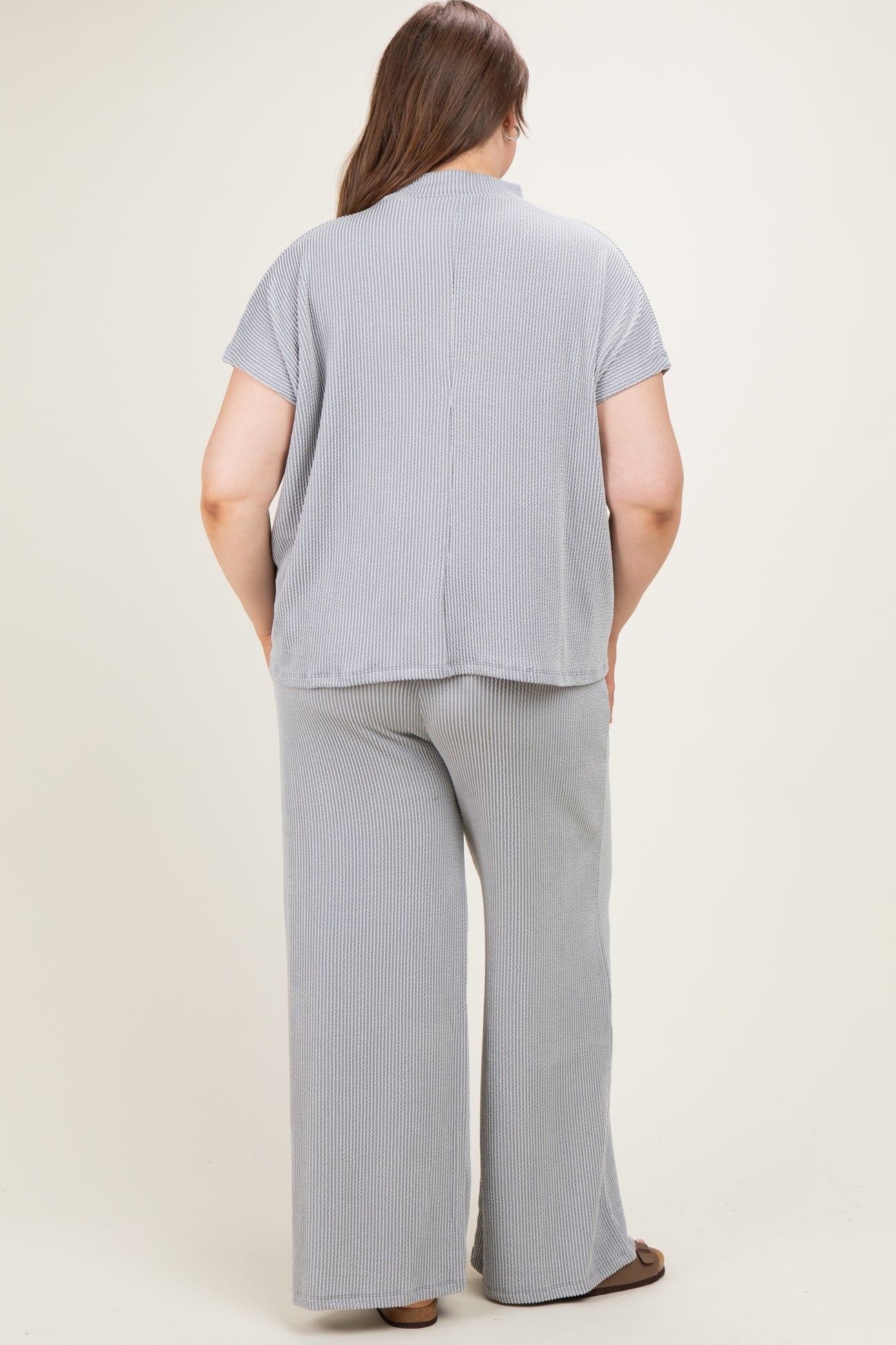 woman wearing a light gray and white striped maternity plus outfit with a loose fit top and wide-leg pants, seen from the back