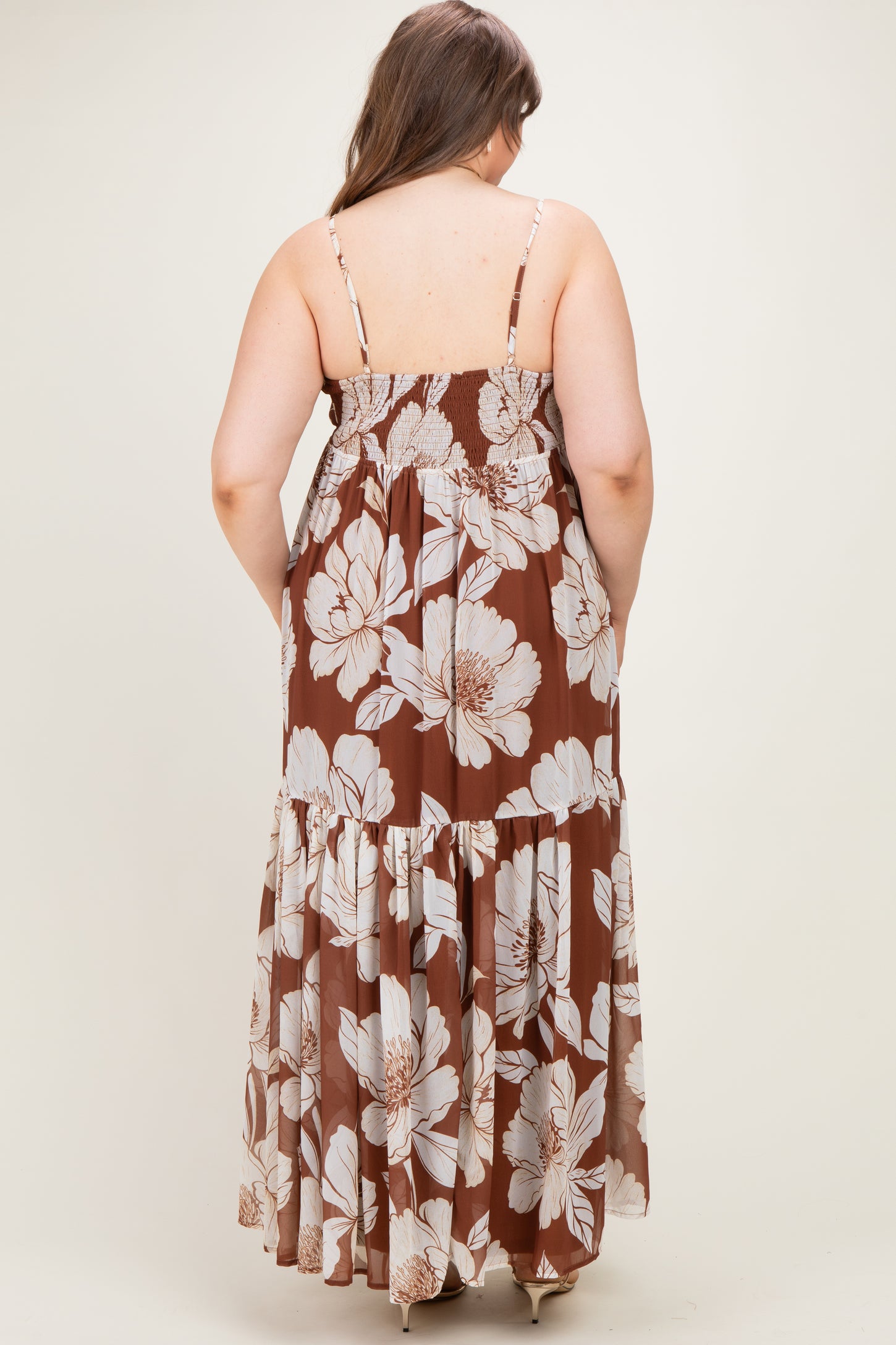 woman wearing a brown floral maternity maxi dress, showing the back view with adjustable straps and tiered skirt