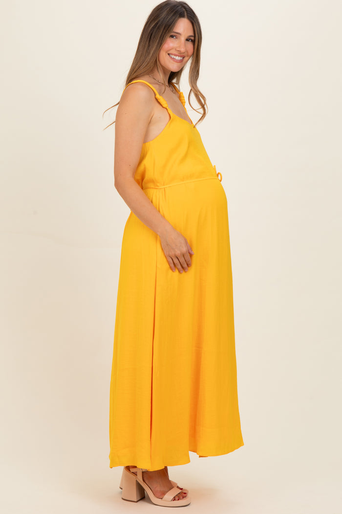 woman wearing a yellow sleeveless maternity maxi dress with a drawstring waist and visible baby bump