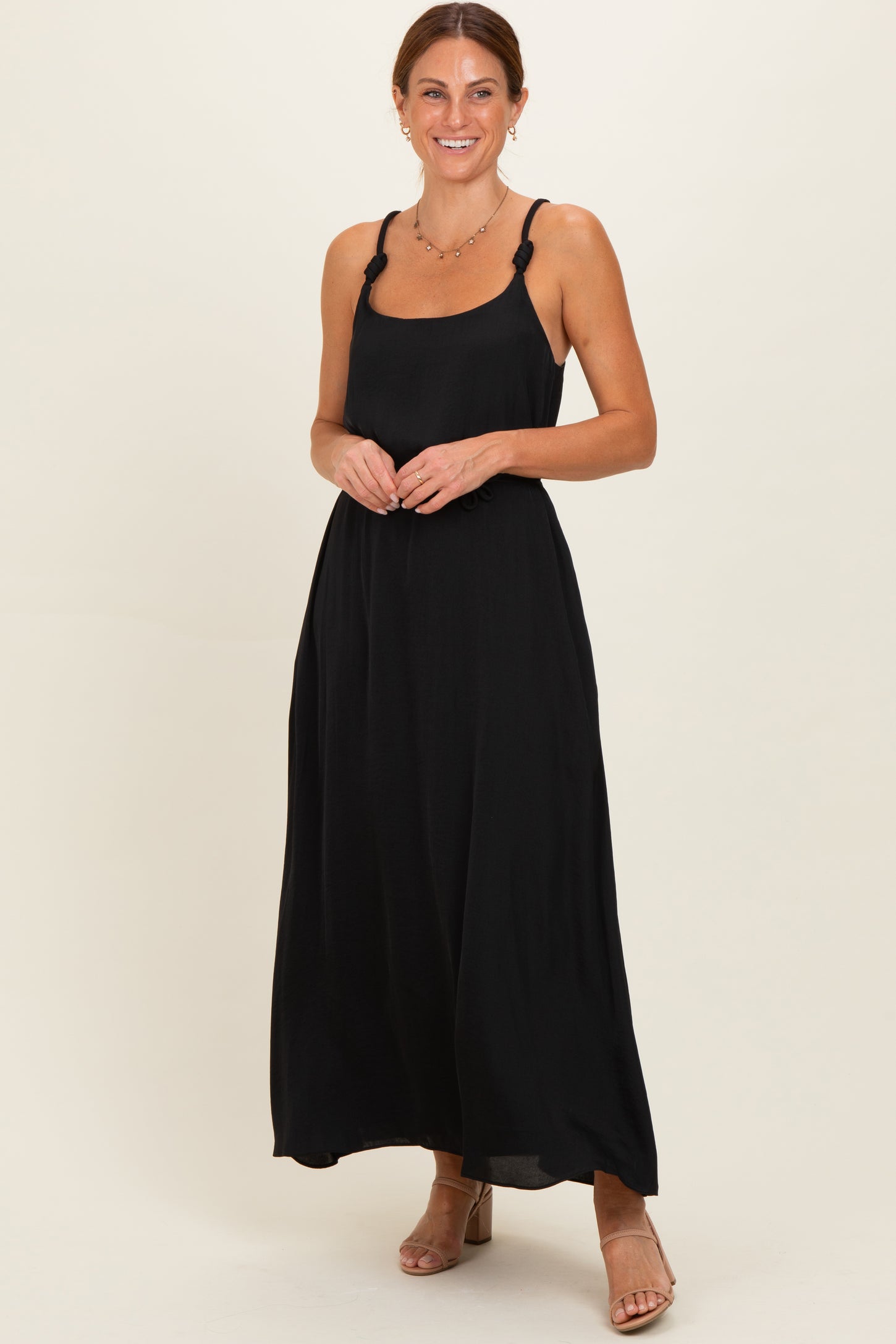 woman wearing a black maxi dress with decorative straps and a relaxed fit, smiling against a light background