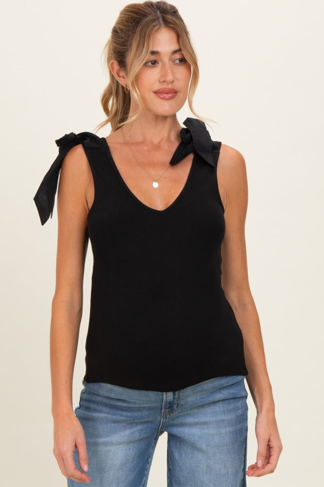 woman wearing a black maternity top with a v-neck and tie shoulder details, paired with blue jeans