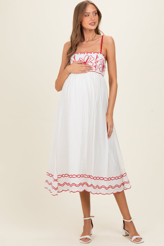 woman wearing a white maternity dress with red floral embroidery and holding her baby bump