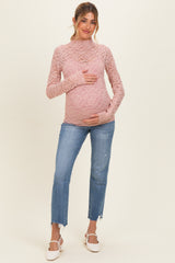 woman wearing a pink lace long sleeve maternity top and holding her baby bump with distressed blue jeans