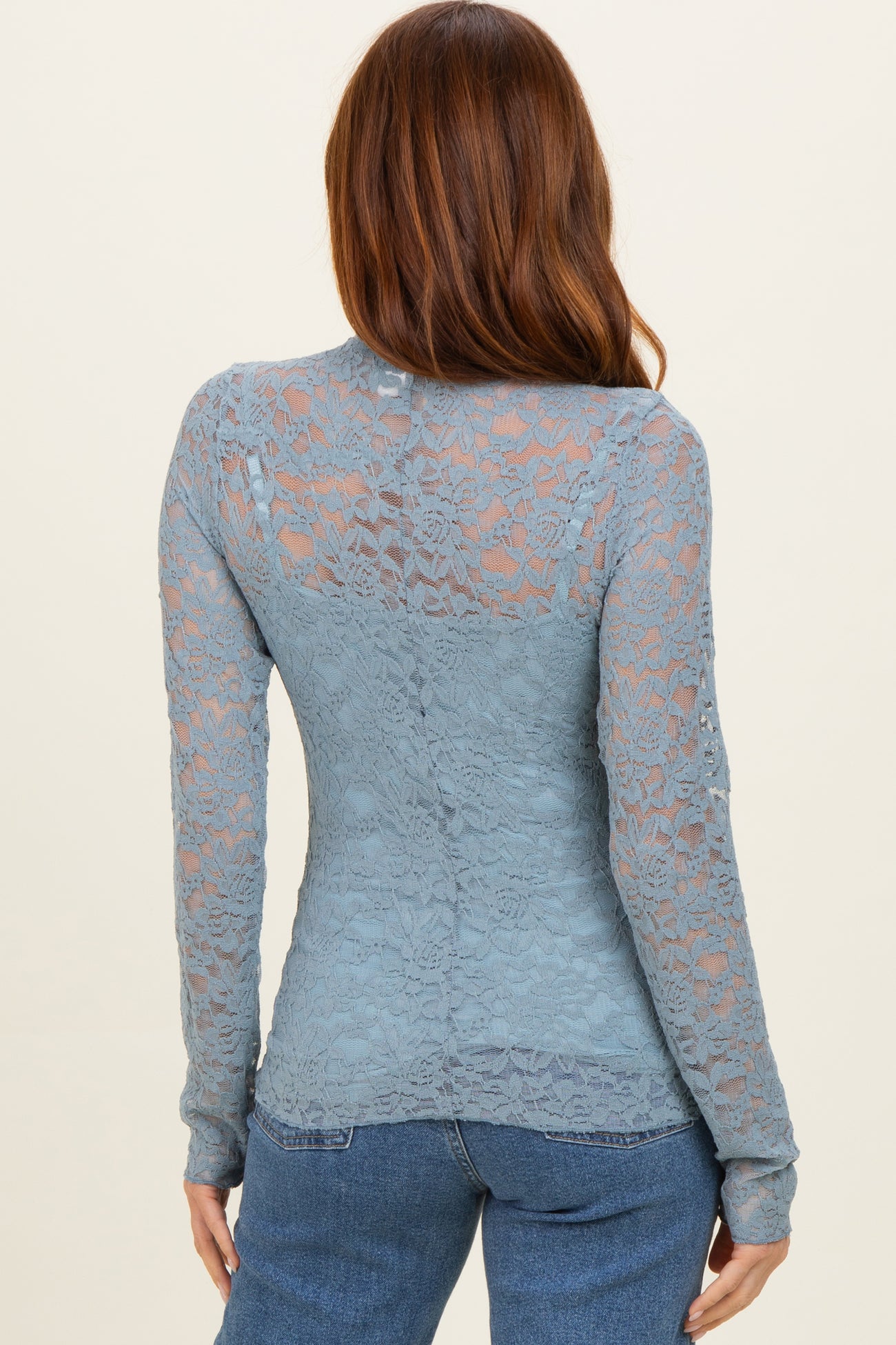 woman wearing a blue lace long sleeve top, shown from the back with floral lace pattern and fitted style