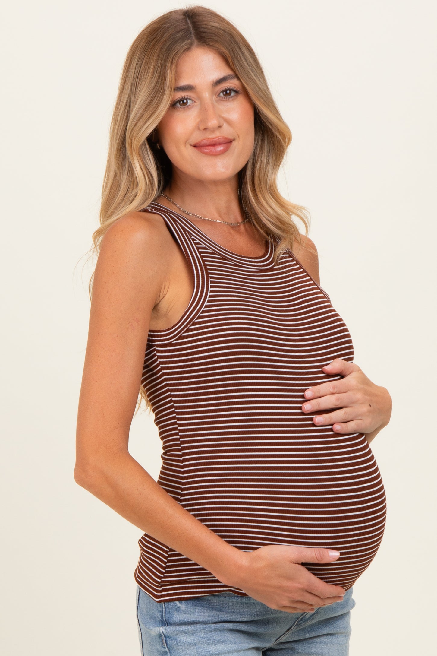 woman wearing a brown and cream striped maternity tank top, holding her baby bump