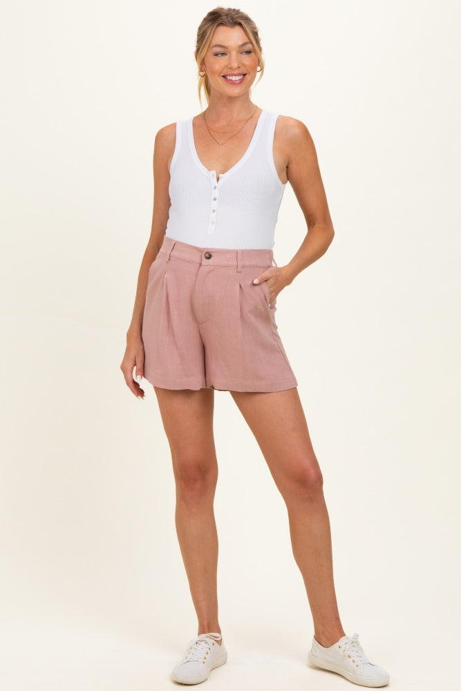 woman wearing a white ribbed sleeveless maternity top and light pink shorts, smiling with hands on her hips
