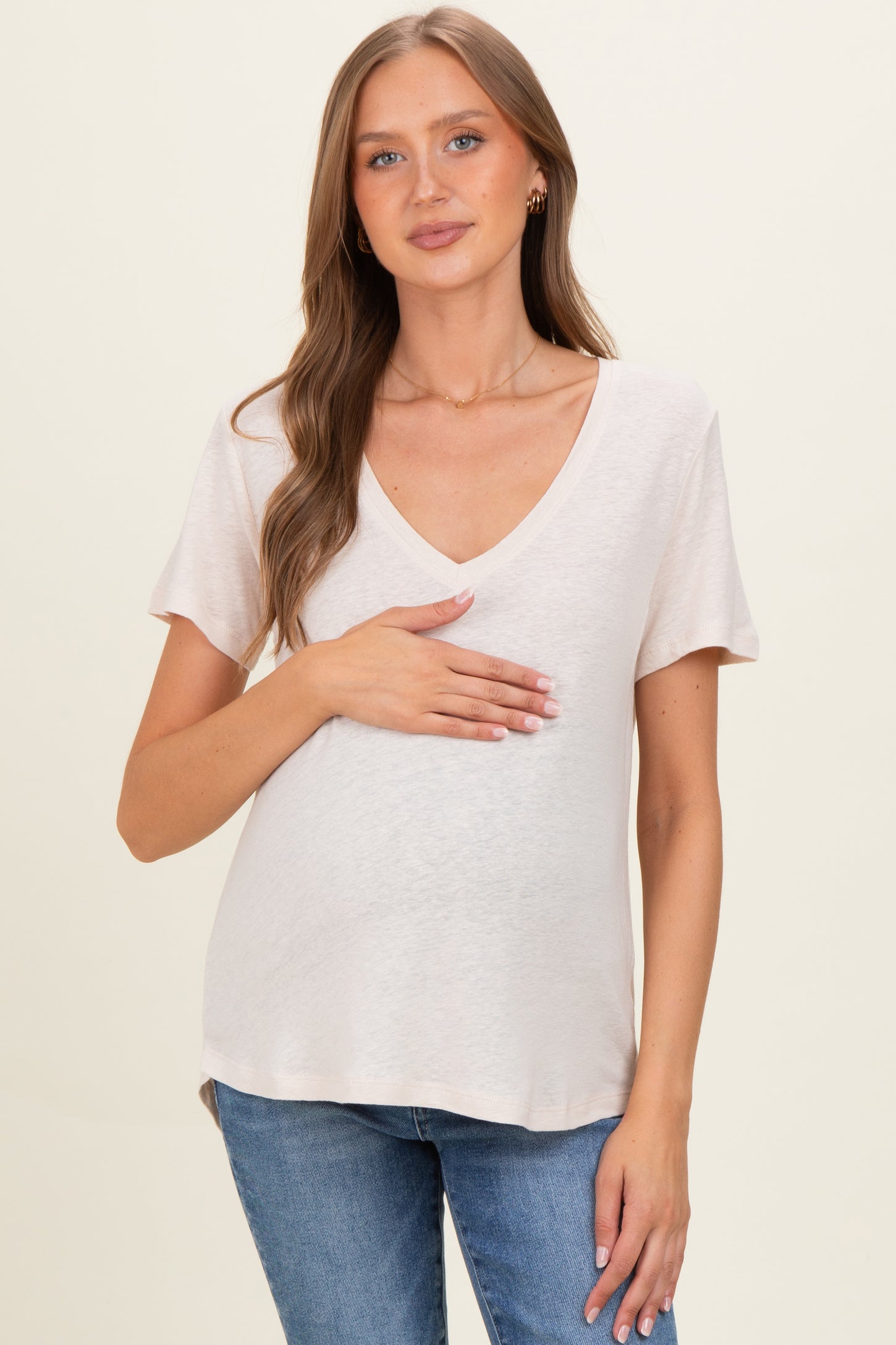 woman wearing a light beige v-neck maternity top and holding her baby bump