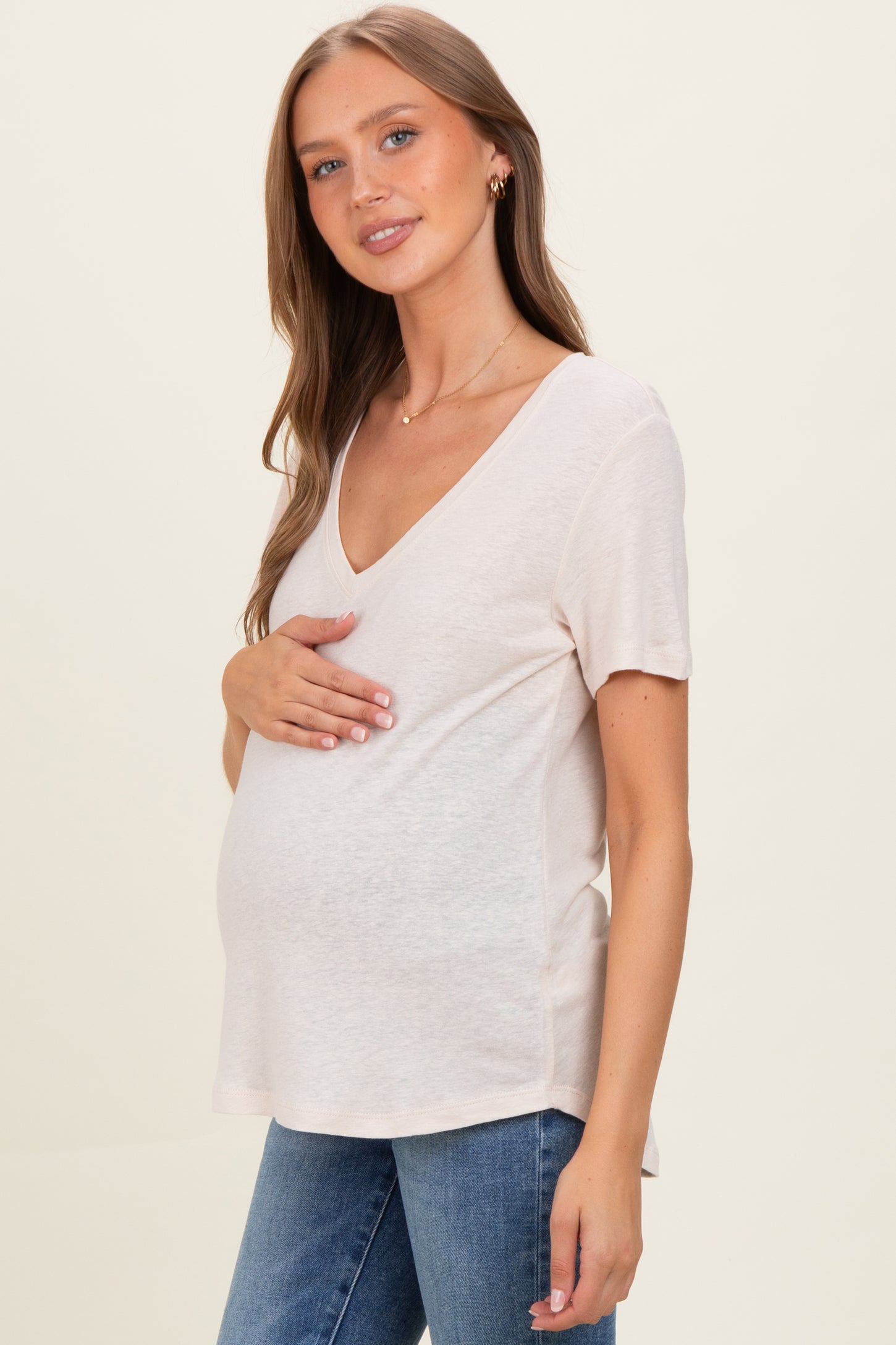 woman wearing a light pink short sleeve maternity top and holding her baby bump while standing sideways