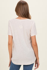 woman wearing a light pink short sleeve maternity top, showing the back and styled with blue jeans
