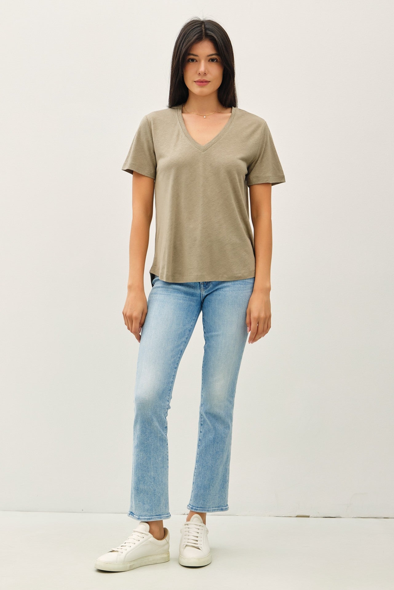 woman wearing a taupe v-neck t-shirt with short sleeves and light blue flared jeans