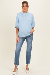 woman wearing a light blue oversized maternity sweater and blue jeans, showcasing her baby bump