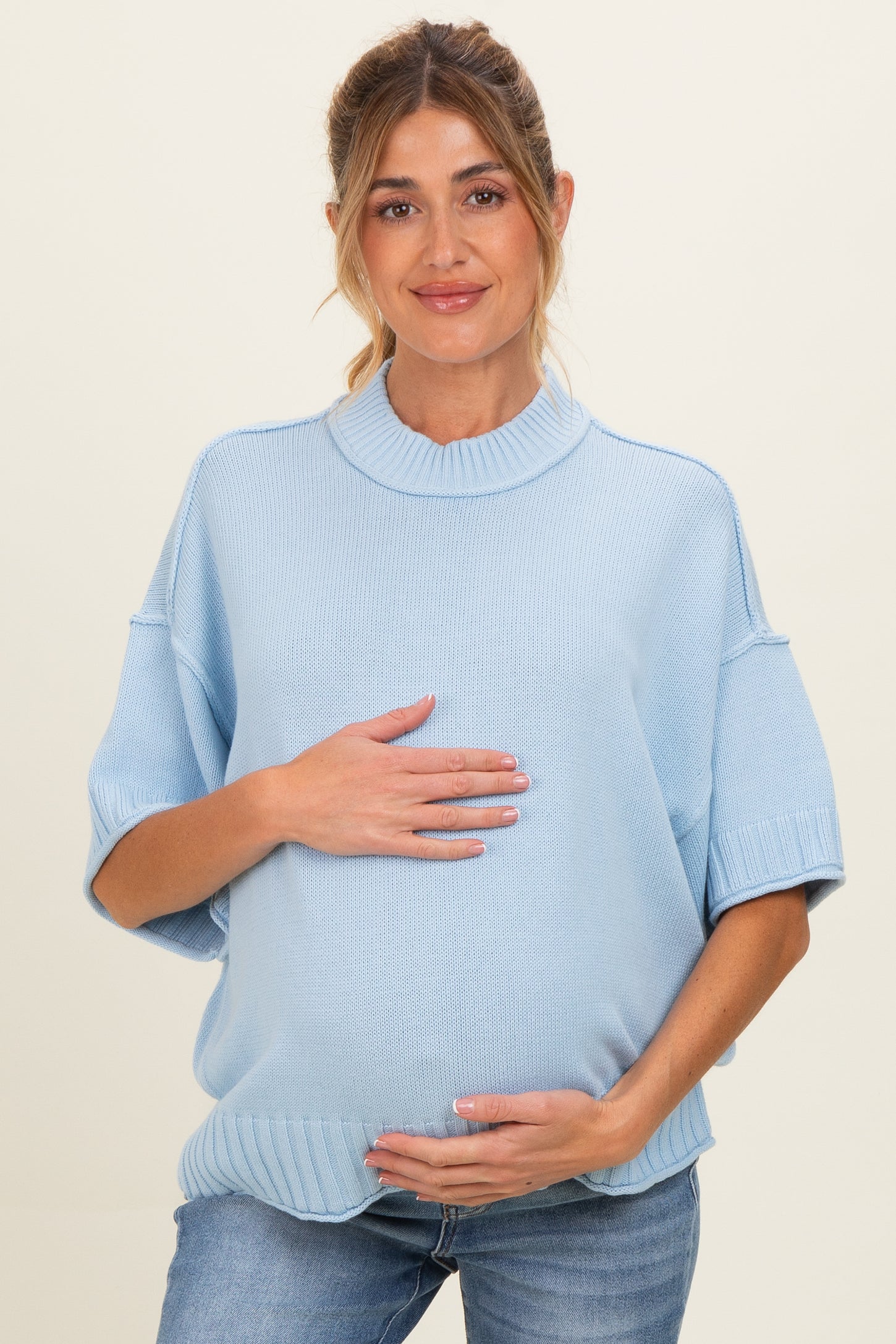 woman wearing a light blue oversized maternity sweater and cradling her baby bump