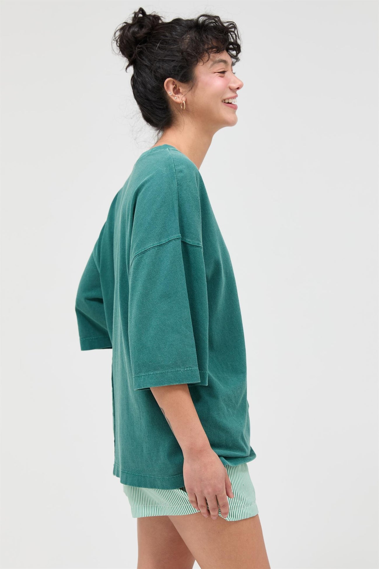 woman wearing a green oversized t-shirt and striped shorts, smiling to the side