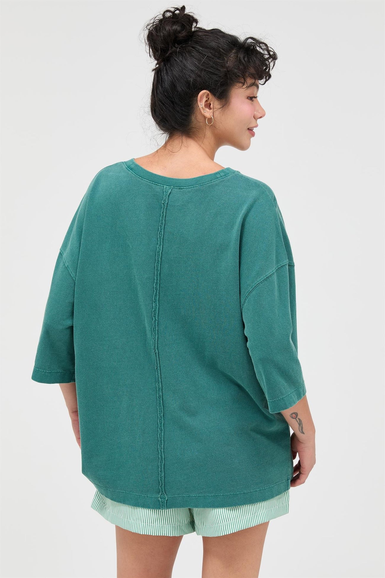 woman wearing a green oversized t-shirt with a seam detail and loose fit, paired with striped shorts