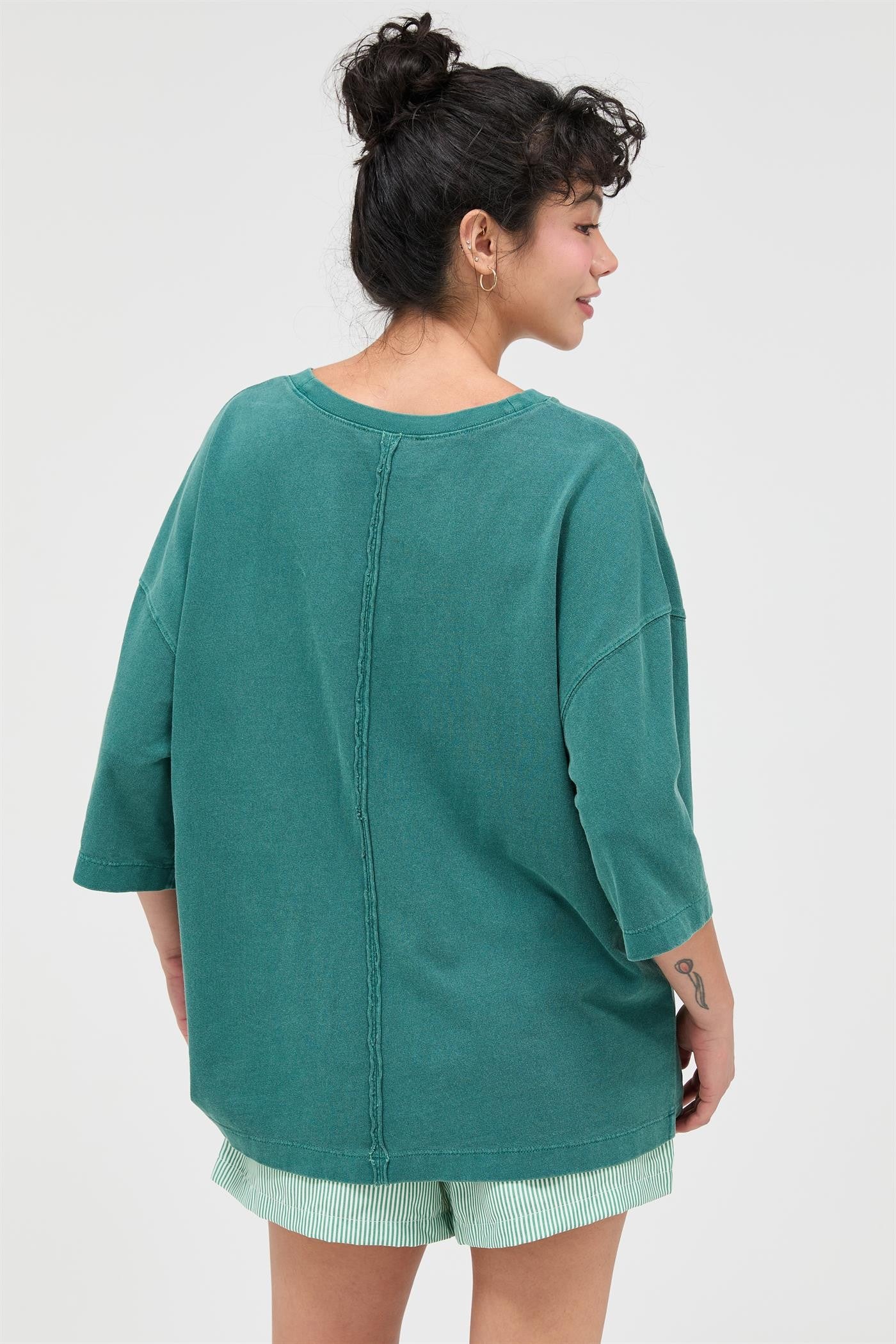 woman wearing a green oversized t-shirt with a seam detail and loose fit, paired with striped shorts