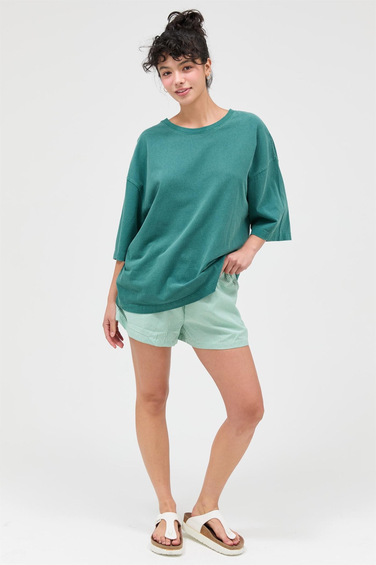 woman wearing a oversized teal sweater and green and white striped shorts, standing on a white background