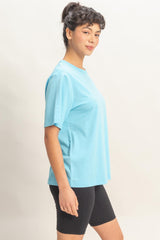 woman wearing a light blue short sleeve t-shirt and black cycling shorts, standing sideways with a smile