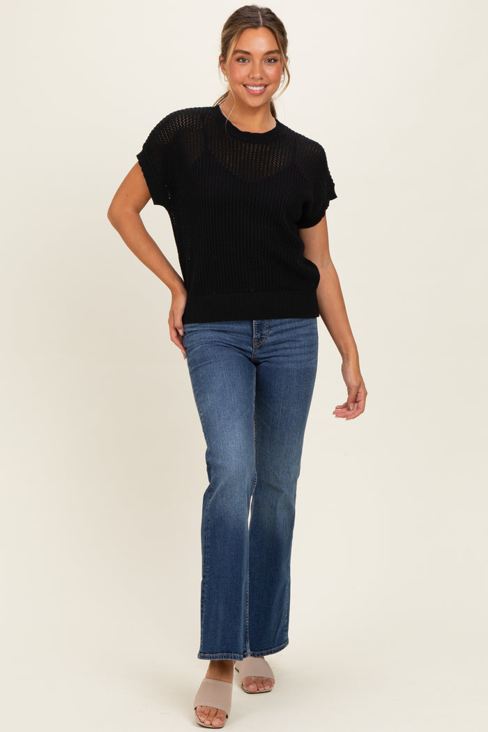 woman wearing a black short sleeve knit top and blue flared jeans, posing with one hand on her hip