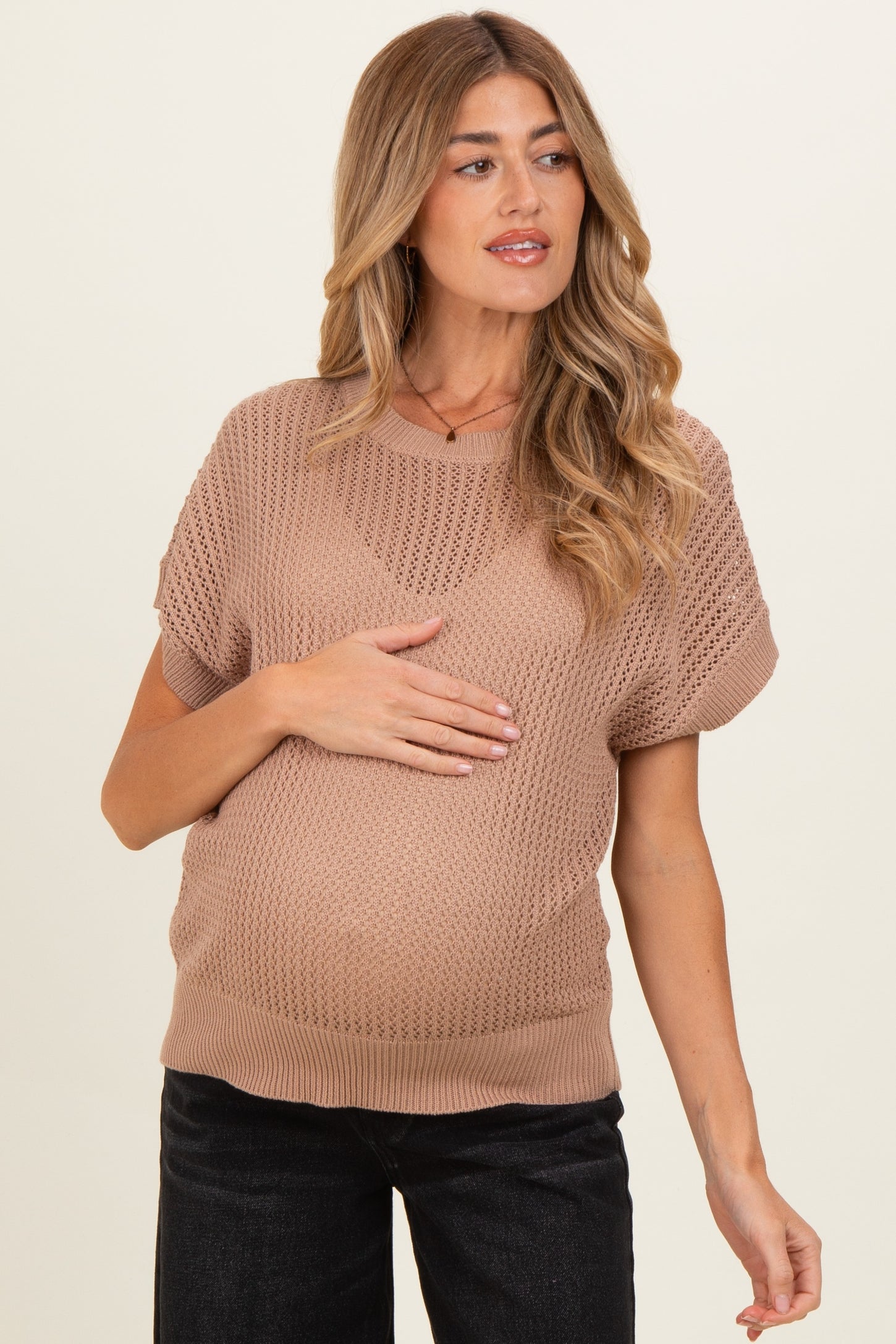 woman wearing a taupe open knit maternity sweater and showing her baby bump