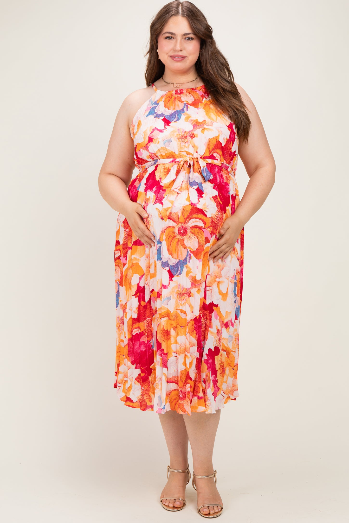 woman wearing a floral print maternity dress in orange and pink tones, gently holding her baby bump