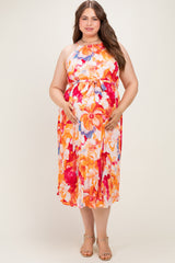 woman wearing a floral print maternity dress in orange and pink tones, gently holding her baby bump