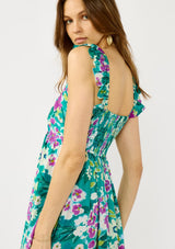 woman wearing a floral print teal sundress with ruffled straps and a smocked back, facing away from the camera