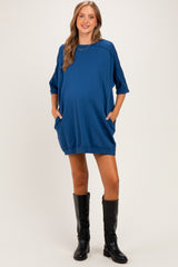 woman wearing a blue oversized maternity dress with pockets and a round neckline, showing her baby bump