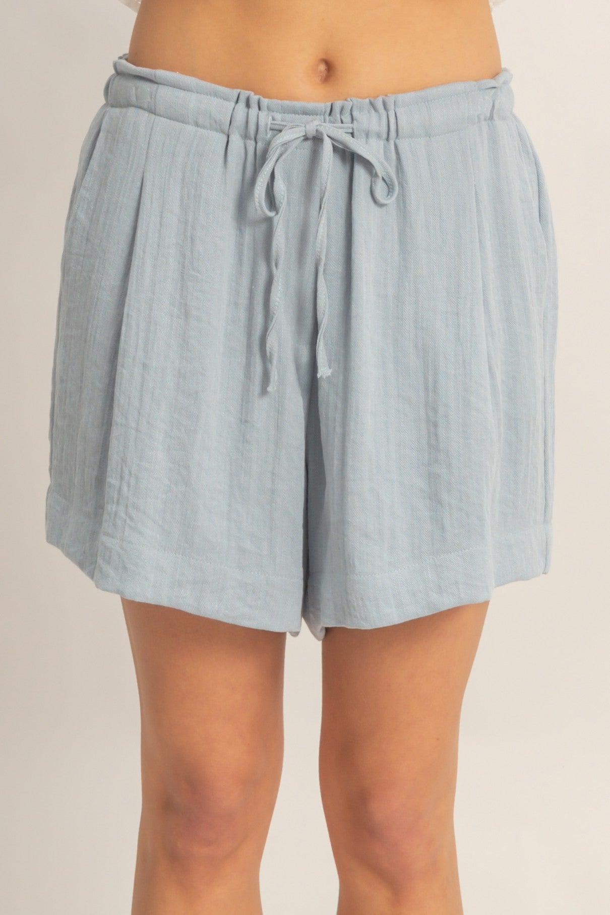 woman wearing light blue linen drawstring shorts with pleat details