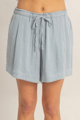woman wearing light blue linen drawstring shorts with pleat details