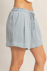 woman wearing light blue high-waisted pleated shorts with a drawstring waist