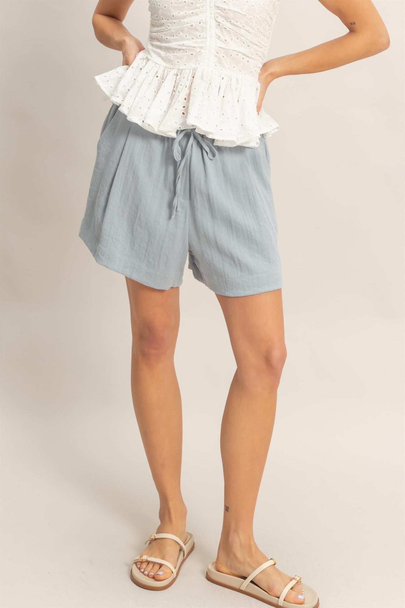 woman wearing light blue drawstring shorts and a white peplum top, standing with one leg slightly forward