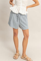 woman wearing light blue drawstring shorts and a white peplum top, standing with one leg slightly forward