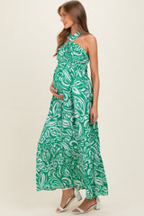 woman wearing a green and white patterned maternity maxi dress with a halter neck and holding her baby bump
