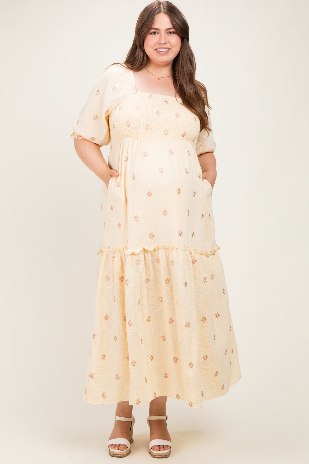 woman wearing a yellow floral maternity dress with short puff sleeves and a tiered skirt, holding her baby bump