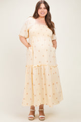 woman wearing a yellow floral maternity dress with short puff sleeves and a tiered skirt, holding her baby bump