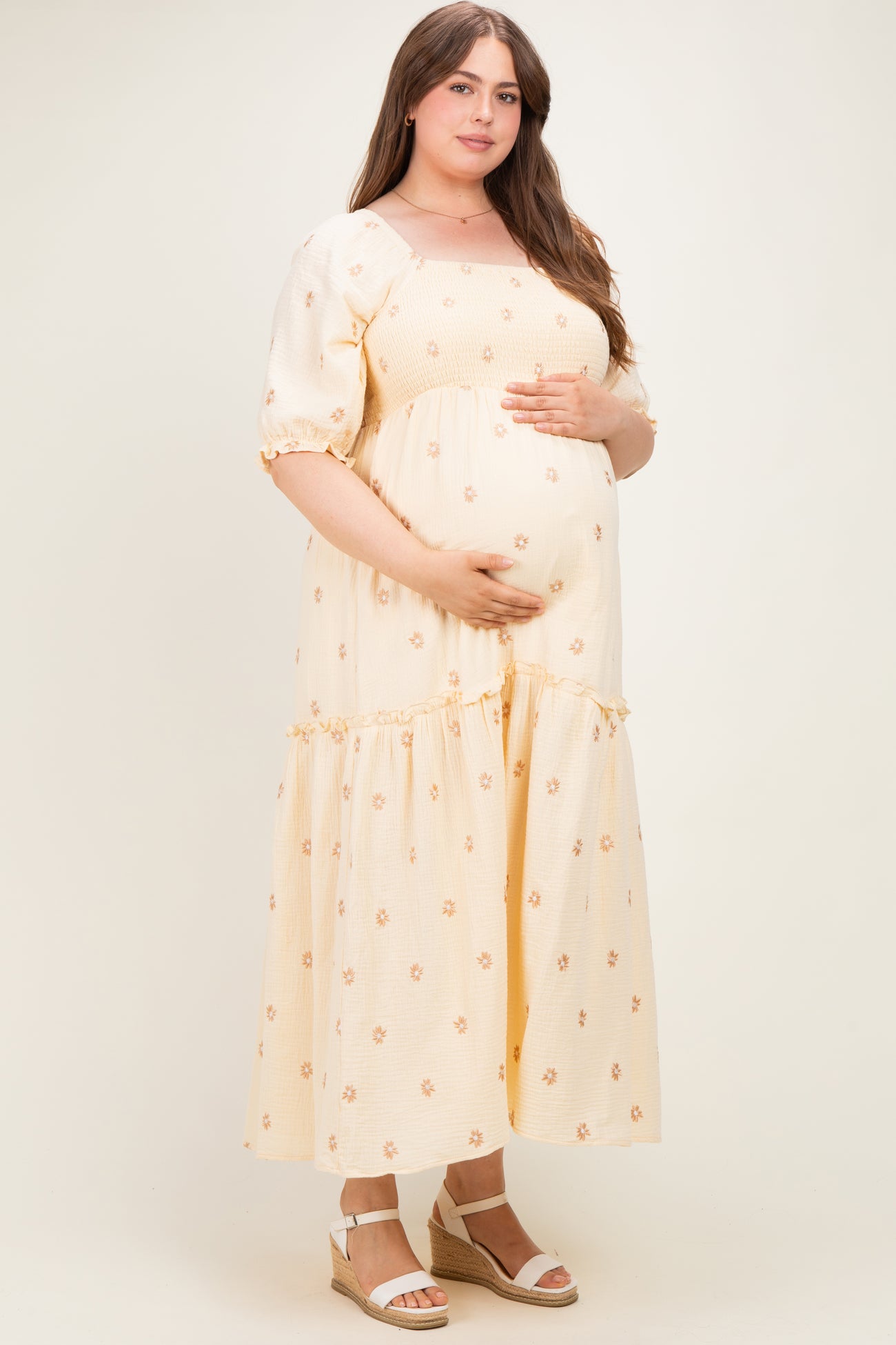 woman wearing a yellow floral print maternity maxi dress and holding her baby bump